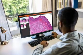 A man working from home on digital pathology images with a monitor on his desk.